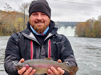 Guided trout fishing on Lake Taneycomo, Branson Missouri – client holding rainbow trout in front of Table Rock Dam
